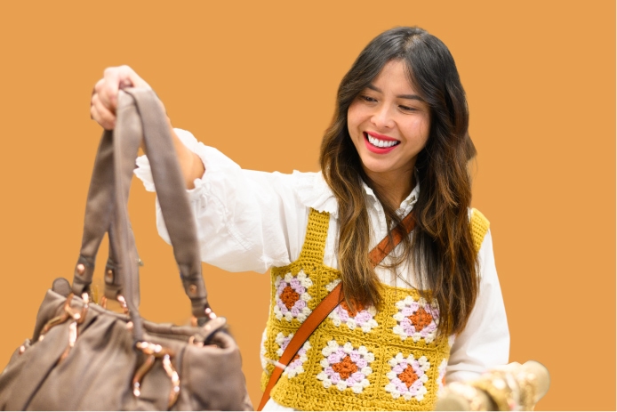 Smiling woman holding a beige handbag in front of an orange backdrop.