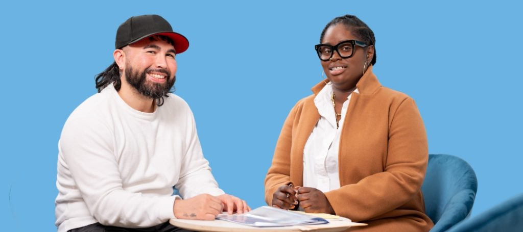 Smiling man and woman review documents at a table against a solid blue background.